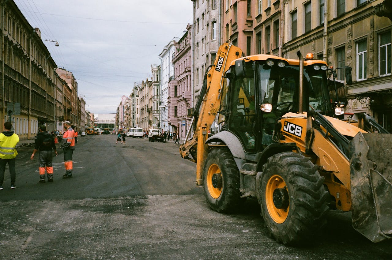 journey-01 City street construction scene with workers and JCB excavator.